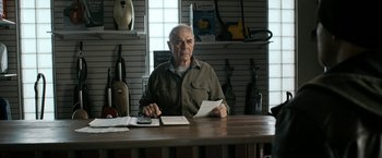 Movie still from “El Camino: A Breaking Bad Movie” (2019), directed by Vince Gilligan – An older man sitting at a table with papers; Medium shot, Low angle