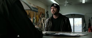 Movie still from “El Camino: A Breaking Bad Movie” (2019), directed by Vince Gilligan – A man sitting at a table in front of a bunch of tools; Medium shot, Over the shoulder angle