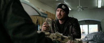 Movie still from “El Camino: A Breaking Bad Movie” (2019), directed by Vince Gilligan – A man sitting at a table holding a stack of money; Close Up shot, Over the shoulder angle