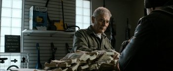 Movie still from “El Camino: A Breaking Bad Movie” (2019), directed by Vince Gilligan – An older man is looking at a pile of money; Medium shot, Over the shoulder angle