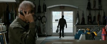 Movie still from “El Camino: A Breaking Bad Movie” (2019), directed by Vince Gilligan – A man holding a guitar case in front of an open garage door; Wide shot, Over the shoulder angle
