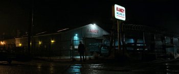 Movie still from “El Camino: A Breaking Bad Movie” (2019), directed by Vince Gilligan – A person standing in front of a building at night; Extreme Wide shot, Low angle
