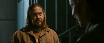 Movie still from “El Camino: A Breaking Bad Movie” (2019), directed by Vince Gilligan – A man with long hair and a beard is standing; Close Up shot, Over the shoulder angle
