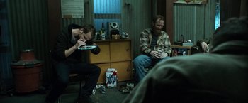 Movie still from “El Camino: A Breaking Bad Movie” (2019), directed by Vince Gilligan – Two men sitting in a living room eating food; Medium shot, High angle