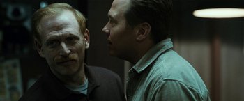 Movie still from “El Camino: A Breaking Bad Movie” (2019), directed by Vince Gilligan – Two men standing next to each other in front of a wall; Close Up shot, Over the shoulder angle