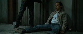 Movie still from “El Camino: A Breaking Bad Movie” (2019), directed by Vince Gilligan – A man sitting on the ground with blood on his shirt; Medium shot, High angle