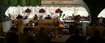 Movie still from “El Camino: A Breaking Bad Movie” (2019), directed by Vince Gilligan – A group of people sitting at a table in a restaurant; Wide shot, High angle
