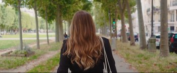 Movie still from “Everybody Loves Jeanne” (2022), directed by Céline Devaux – A woman walking down a sidewalk with long hair; Medium shot, Over the shoulder angle