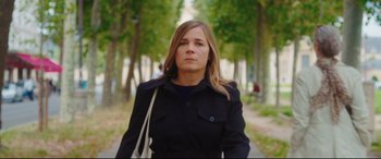 Movie still from “Everybody Loves Jeanne” (2022), directed by Céline Devaux – A woman in a black jacket walking down a street; Medium shot, Low angle