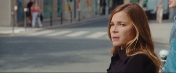 Movie still from “Everybody Loves Jeanne” (2022), directed by Céline Devaux – A woman standing on the side of the street; Close Up shot, Over the shoulder angle