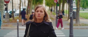 Movie still from “Everybody Loves Jeanne” (2022), directed by Céline Devaux – A woman is walking down the street in a black coat; Medium shot, Low angle