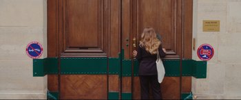 Movie still from “Everybody Loves Jeanne” (2022), directed by Céline Devaux – A woman standing in front of a wooden door; Medium shot, Over the shoulder angle