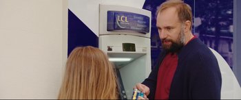 Movie still from “Everybody Loves Jeanne” (2022), directed by Céline Devaux – A man and a woman standing in front of an atm machine; Medium shot, Over the shoulder angle