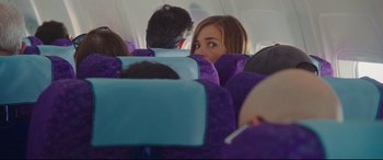 Movie still from “Everybody Loves Jeanne” (2022), directed by Céline Devaux – A woman sitting on a seat on an airplane; Medium shot, Over the shoulder angle