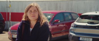 Movie still from “Everybody Loves Jeanne” (2022), directed by Céline Devaux – A woman standing in front of a parked red car; Medium shot, Low angle