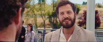 Movie still from “Everybody Loves Jeanne” (2022), directed by Céline Devaux – A man with a beard is smiling for the camera; Close Up shot, Over the shoulder angle