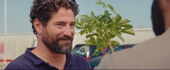 Movie still from “Everybody Loves Jeanne” (2022), directed by Céline Devaux – A man with a beard and a plant in the background; Close Up shot, Over the shoulder angle
