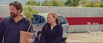 Movie still from “Everybody Loves Jeanne” (2022), directed by Céline Devaux – A woman in a purple sweater standing next to a car; Medium shot, Over the shoulder angle