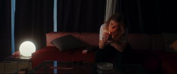 Movie still from “Everybody Loves Jeanne” (2022), directed by Céline Devaux – A woman sitting on a couch with a cigarette in her mouth; Medium shot, High angle