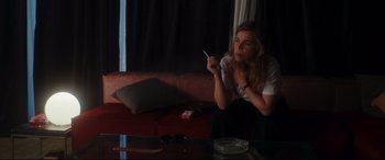 Movie still from “Everybody Loves Jeanne” (2022), directed by Céline Devaux – A woman sitting on a couch holding a cigarette; Medium shot, Over the shoulder angle