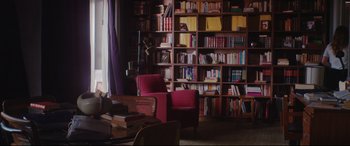 Movie still from “Everybody Loves Jeanne” (2022), directed by Céline Devaux – A living room filled with furniture next to a book shelf filled with lots of books; Wide shot, High angle