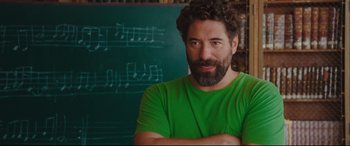 Movie still from “Everybody Loves Jeanne” (2022), directed by Céline Devaux – A man with a beard is standing in front of a chalkboard; Close Up shot, Over the shoulder angle