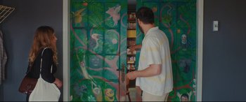 Movie still from “Everybody Loves Jeanne” (2022), directed by Céline Devaux – A man standing in front of a wall with many paintings on it; Medium shot, Low angle