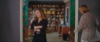 Movie still from “Everybody Loves Jeanne” (2022), directed by Céline Devaux – A woman standing in front of bookshelves with her arms crossed; Medium shot, High angle