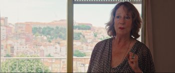 Movie still from “Everybody Loves Jeanne” (2022), directed by Céline Devaux – A woman standing in front of a window with a city view; Close Up shot, Over the shoulder angle