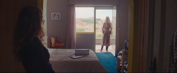 Movie still from “Everybody Loves Jeanne” (2022), directed by Céline Devaux – A woman standing in a bedroom looking out a sliding glass door; Wide shot, Over the shoulder angle