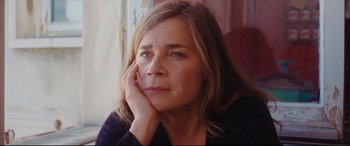 Movie still from “Everybody Loves Jeanne” (2022), directed by Céline Devaux – A person sitting with her hand on her face; Close Up shot, Low angle