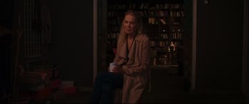 Movie still from “Everybody Loves Jeanne” (2022), directed by Céline Devaux – A woman sitting in front of bookshelves holding a cup; Medium shot, Over the shoulder angle
