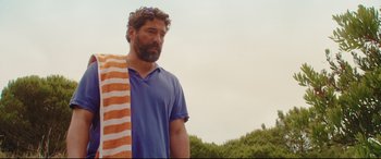 Movie still from “Everybody Loves Jeanne” (2022), directed by Céline Devaux – A man with a beard standing next to an orange towel; Medium shot, Over the shoulder angle