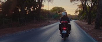 Movie still from “Everybody Loves Jeanne” (2022), directed by Céline Devaux – Two people riding a motorcycle down a street; Wide shot, Low angle