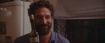 Movie still from “Everybody Loves Jeanne” (2022), directed by Céline Devaux – A man holding a bottle of wine in his right hand; Close Up shot, Over the shoulder angle