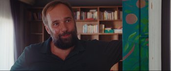 Movie still from “Everybody Loves Jeanne” (2022), directed by Céline Devaux – A man with a goatee is smiling for the camera; Close Up shot, Over the shoulder angle