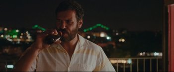 Movie still from “Everybody Loves Jeanne” (2022), directed by Céline Devaux – A man with a beard is holding a bottle of soda; Medium shot, Over the shoulder angle