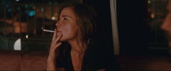 Movie still from “Everybody Loves Jeanne” (2022), directed by Céline Devaux – A woman sitting in front of a window smoking a cigarette; Close Up shot, Over the shoulder angle