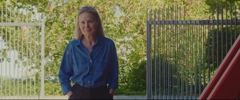 Movie still from “Everybody Loves Jeanne” (2022), directed by Céline Devaux – An older woman standing in front of a gate; Medium shot, Low angle