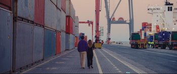 Movie still from “Everybody Loves Jeanne” (2022), directed by Céline Devaux – Two people walking down a street near a crane; Wide shot, High angle