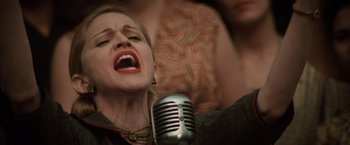 Movie still from “Evita” (1996), directed by Alan Parker – A woman singing into a microphone in front of other people; Close Up shot, Overhead angle