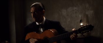 Movie still from “Evita” (1996), directed by Alan Parker – A man in a suit and tie holding a guitar; Medium shot, Low angle