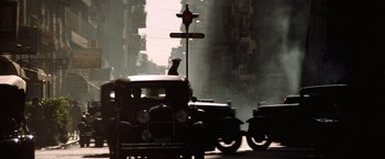 Movie still from “Evita” (1996), directed by Alan Parker – An old car driving down a street past tall buildings; Extreme Wide shot, Low angle