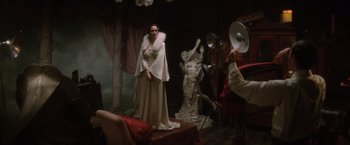 Movie still from “Evita” (1996), directed by Alan Parker – A woman dressed in a white dress standing next to a statue; Wide shot, Over the shoulder angle