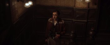 Movie still from “Evita” (1996), directed by Alan Parker – A man holding a camera while standing in front of a wall; Medium shot, High angle