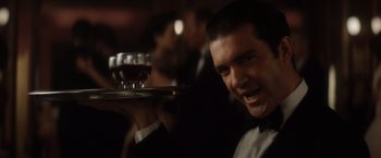 Movie still from “Evita” (1996), directed by Alan Parker – A man holding a tray with a glass of wine on top of it; Close Up shot, Low angle