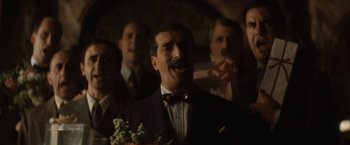 Movie still from “Evita” (1996), directed by Alan Parker – A group of men standing around each other in a dark room; Medium shot, Low angle