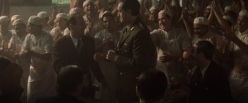 Movie still from “Evita” (1996), directed by Alan Parker – A group of people in a room with a man in a uniform; Medium shot, Low angle