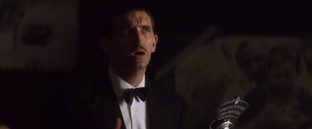 Movie still from “Evita” (1996), directed by Alan Parker – A person wearing a suit and a bow tie; Close Up shot, Low angle