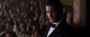 Movie still from “Evita” (1996), directed by Alan Parker – A man in a tuxedo standing in front of a crowd; Close Up shot, Low angle